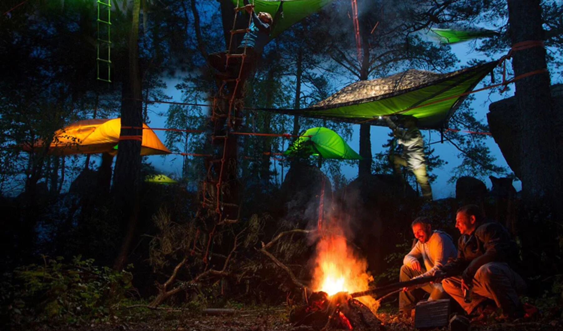 Camp de plusieurs tentes suspendues de nuit avec feu de camp